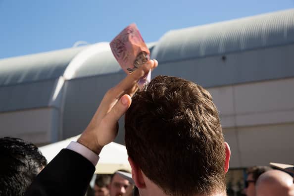 A man holding a $5 note on his head while playing two-up. The money and the positioning indicates that he is betting $5 on heads.