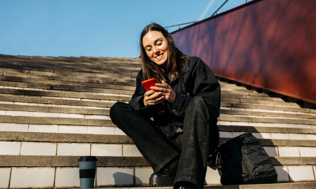 Smiling woman sitting on stairs using a red phone.
