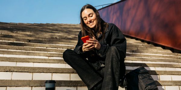 Smiling woman sitting on stairs using a red phone.