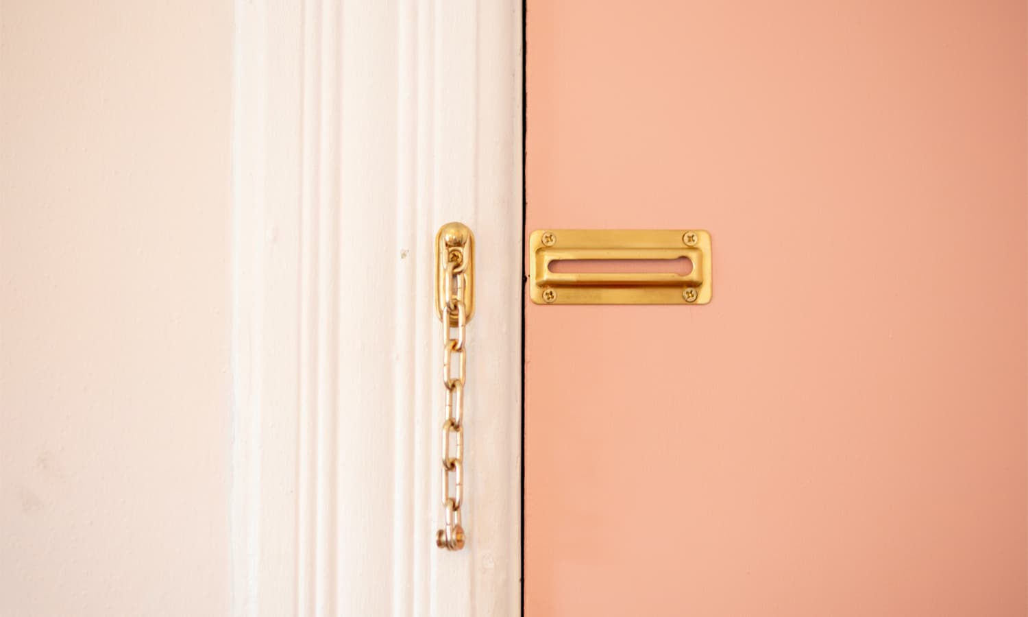 An open door chain lock on a pink door.