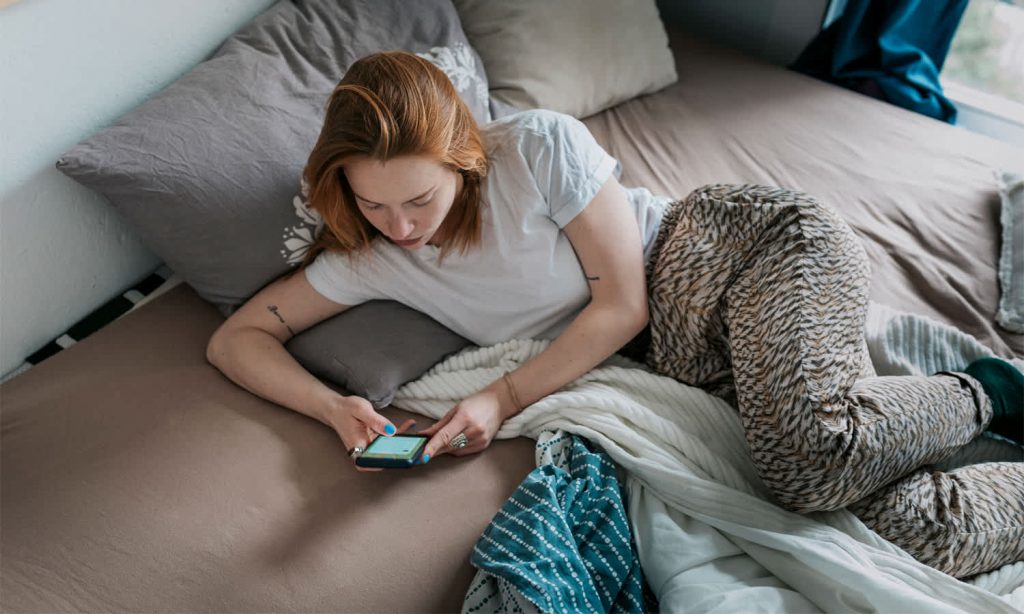 A girl lying on a bed and writing a message on her smartphone.