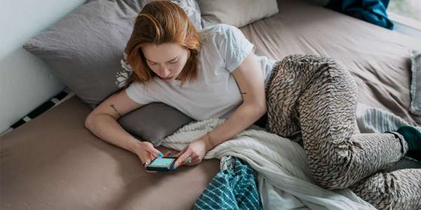 A girl lying on a bed and writing a message on her smartphone.