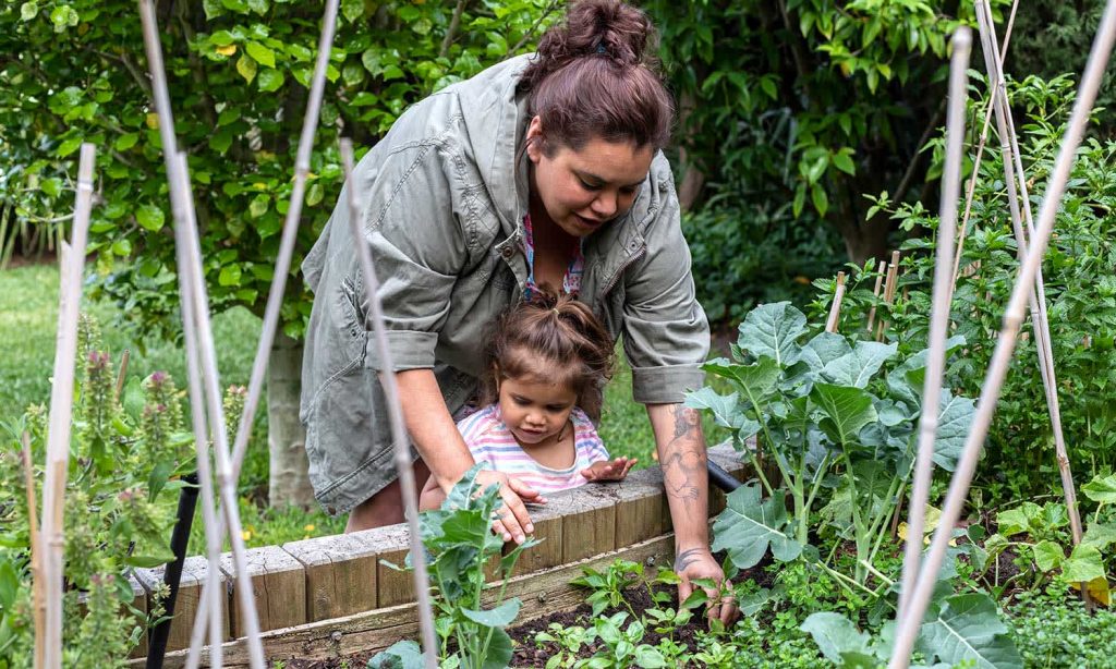 woman tending to a vegetable garden with her child