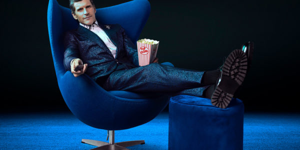 Osher Günsberg in an armchair holding popcorn and a TV remote.