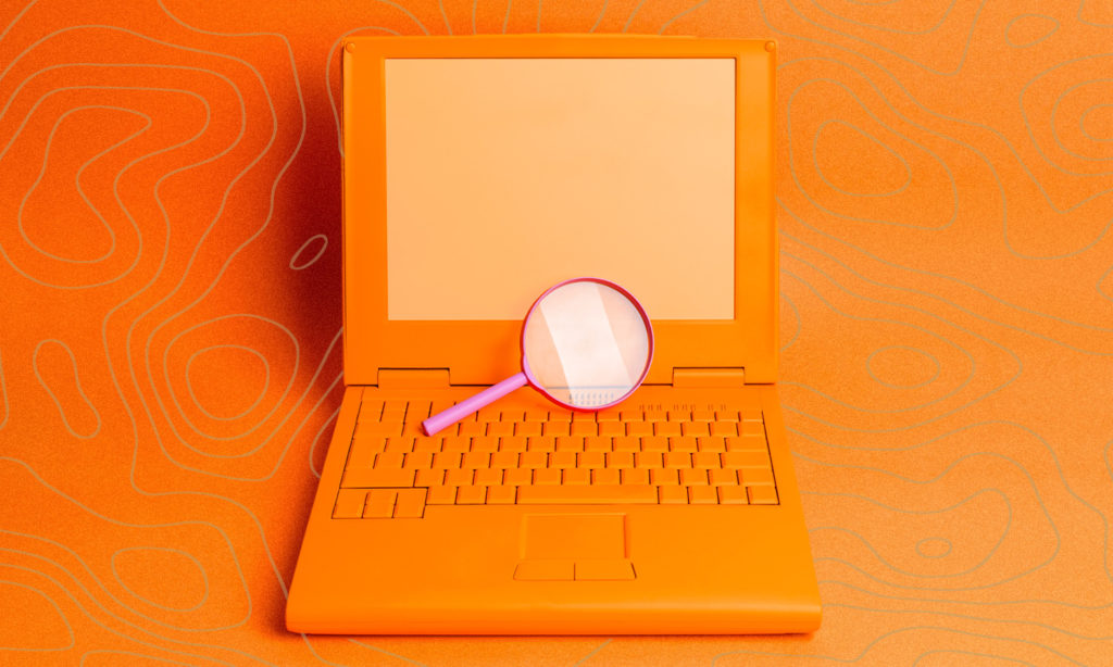 A retro laptop on orange background with a pink magnifying glass in the centre