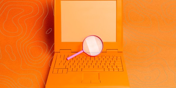 A retro laptop on orange background with a pink magnifying glass in the centre