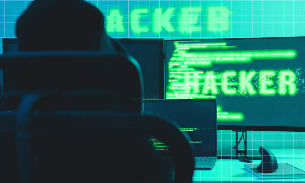 A cheesy image of a hacker sitting at a desk with green test on a computer screen to represent cyber security.