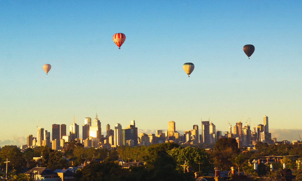 Image shows hot air balloons floating over the Melbourne city skyline.