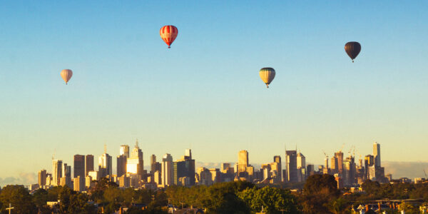 Image shows hot air balloons floating over the Melbourne city skyline.