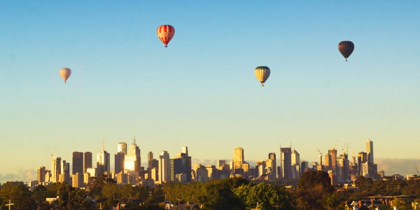 Image shows hot air balloons floating over the Melbourne city skyline.