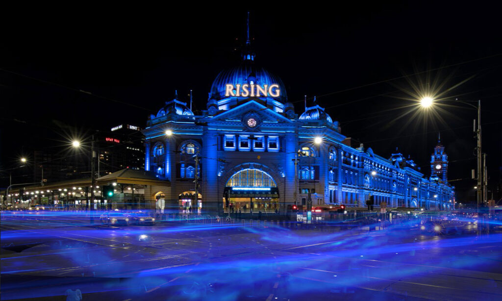 Flinders Street Station lit up in blue with the word Rising on the front to showcase Rising Festival Melbourne.