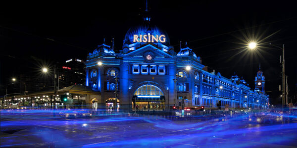 Flinders Street Station lit up in blue with the word Rising on the front to showcase Rising Festival Melbourne.