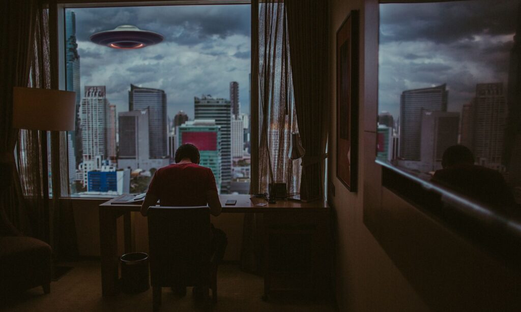 An image showing a ufo floating above a city while a man works.