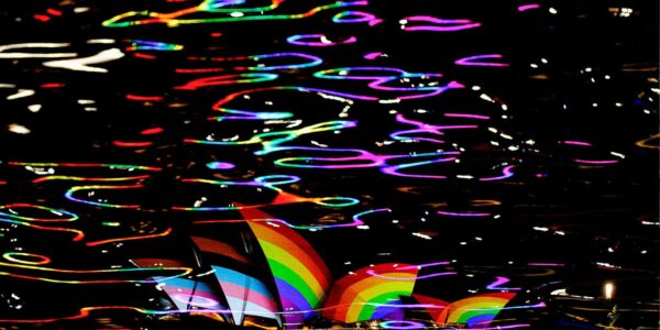 An image of the Opera House in Sydney lit up with the LGBTQIA+ pride flag to illustrate homophobia in Australia