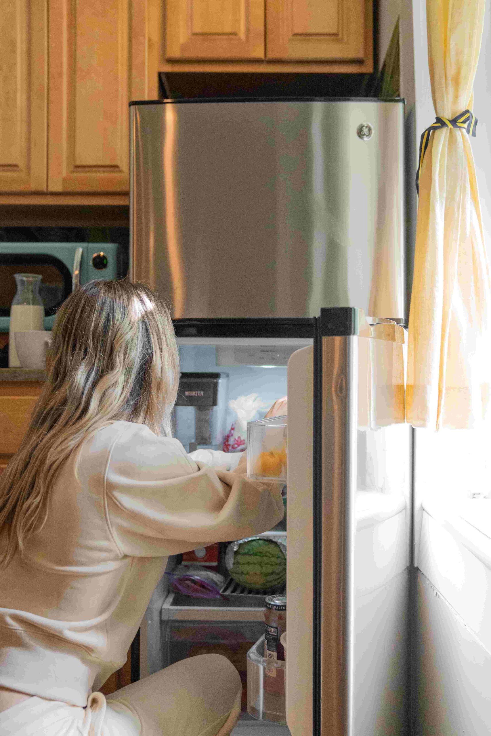 Girl reaching into fridge and taking food out